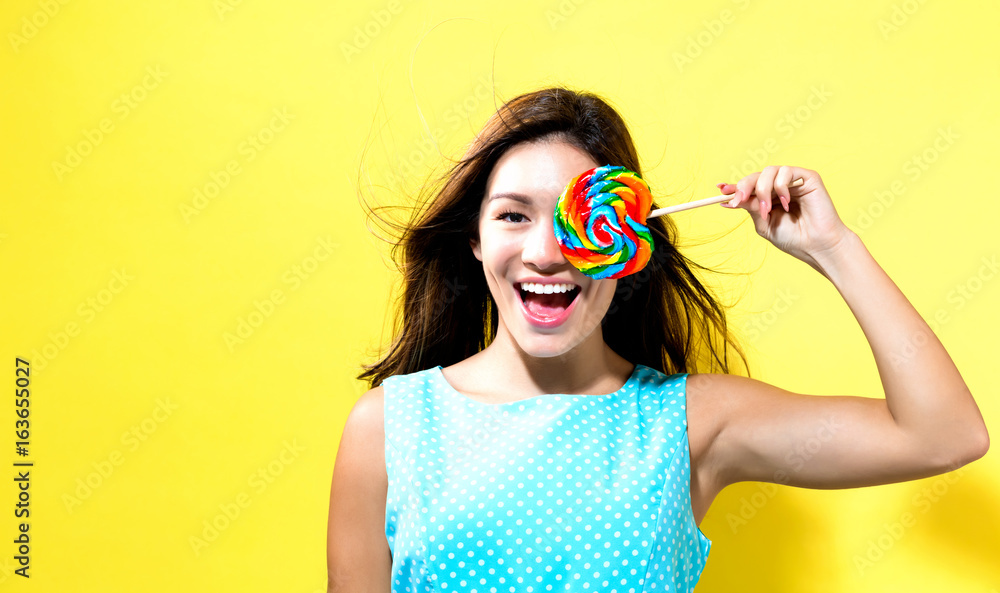 Young woman holding a lollipop on a yellow background