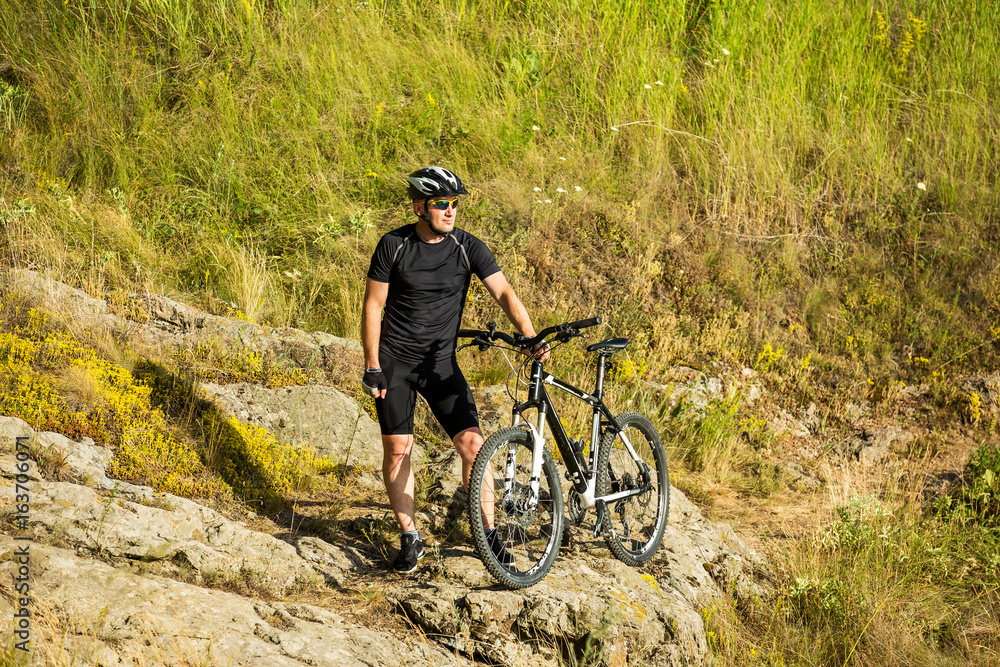 Mountain biker with a bicycle on a rock. Motivation and inspiration for adventure.