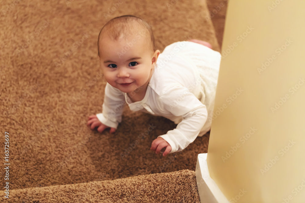 Happy toddler girl climbing up the stairs in her house