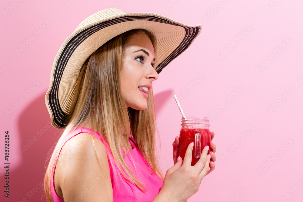 Happy young woman drinking smoothie on a pink background