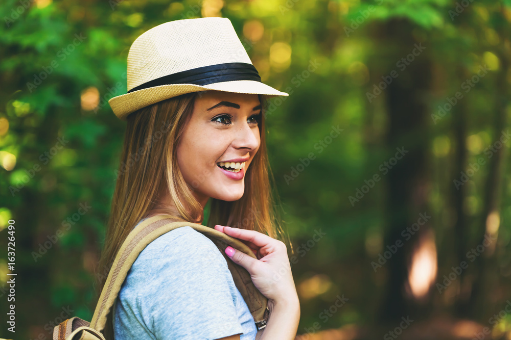 Young woman in the forest with a backpack and hat