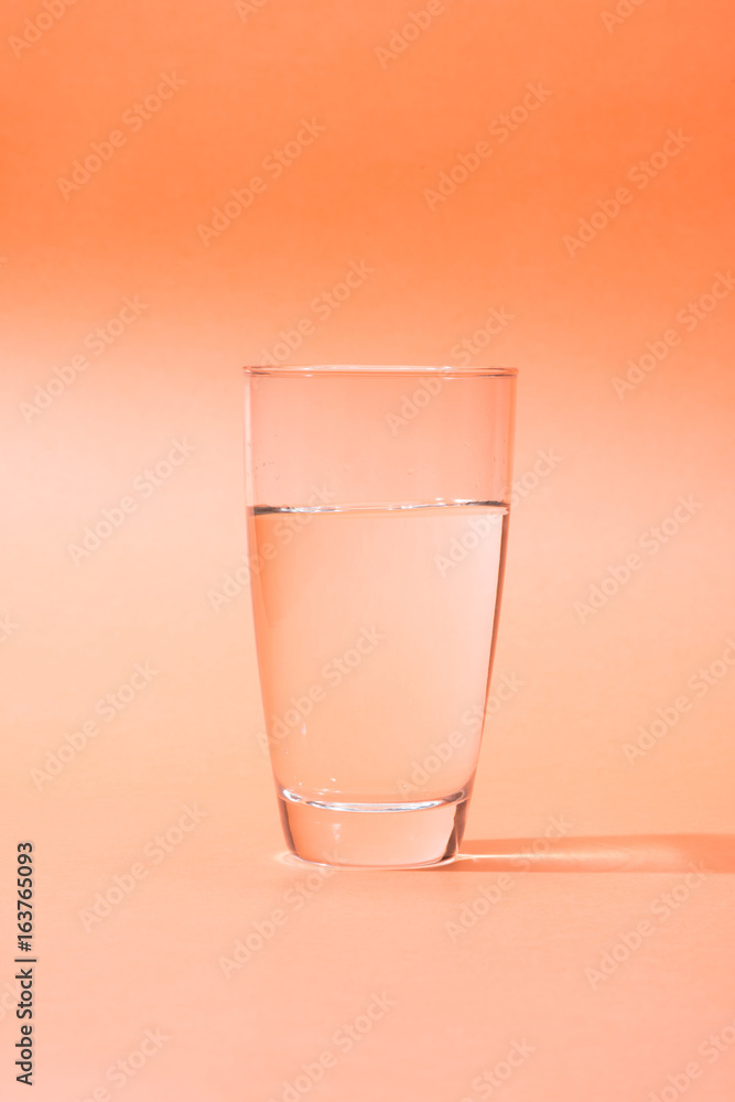 Drinking water in a glass over orange background.