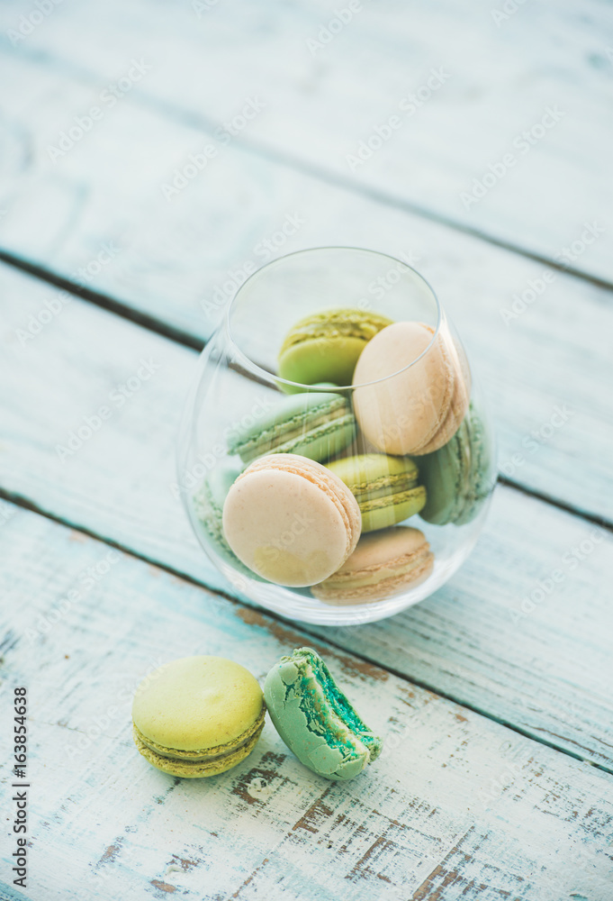 Colorful pastel pink, green and blue French macaron biscuits in glass over light blue painted wooden