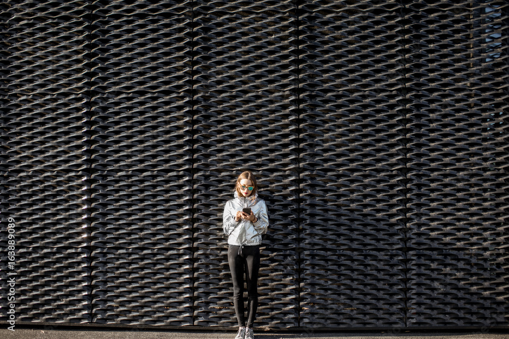 Lifestyle portrait of a stylish woman in silver jacket standing on the modern black wall background