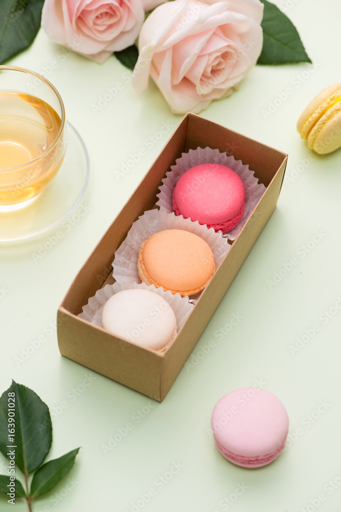 French macaroons. Many variegated sweet macarons in box with bouquet of pink roses on the table