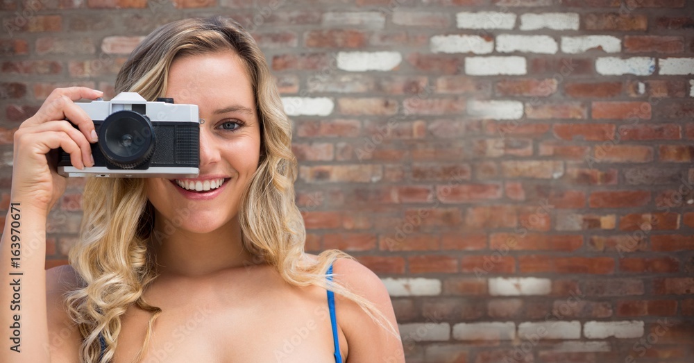 Close up of millennial woman with camera against red brick wall