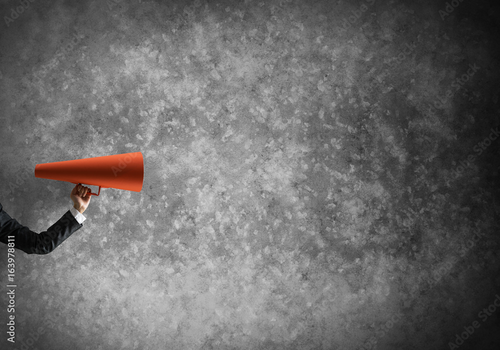 Hand of businesswoman holding red paper trumpet against concrete background