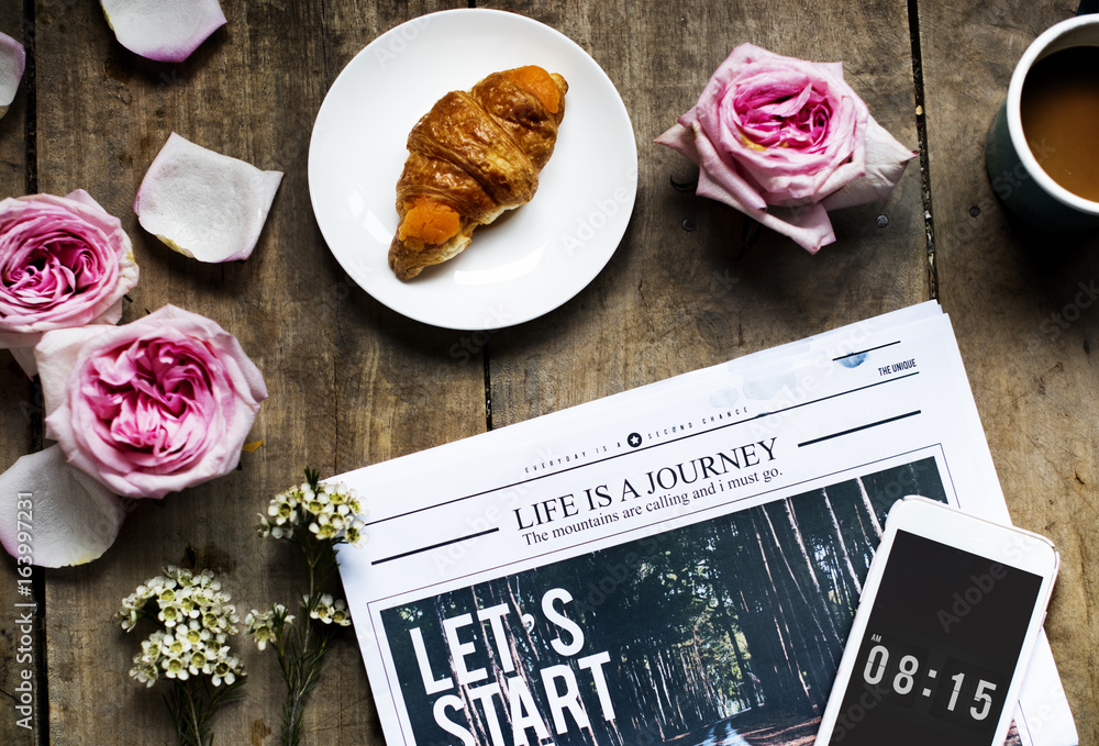 Aerial view of croissant and newspaper with roses decoration on wooden table