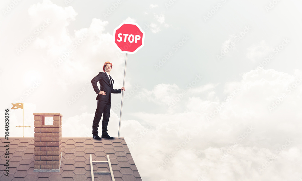 Caucasian businessman on brick house roof showing stop road sign