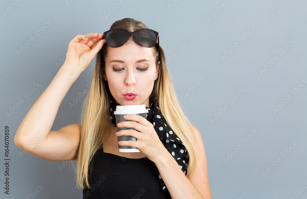 Happy young woman drinking coffee on a gray background