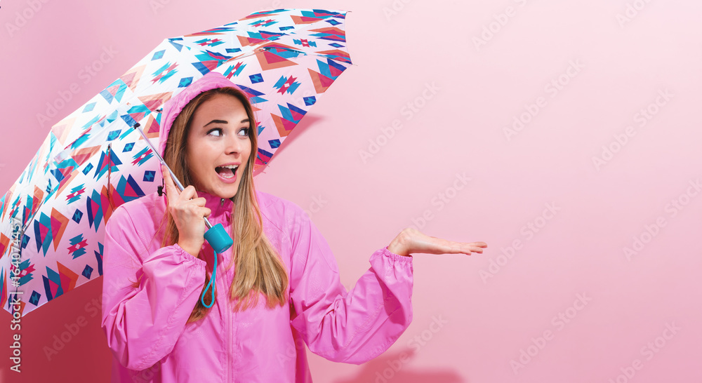 Happy young woman holding an umbrella on a pink background