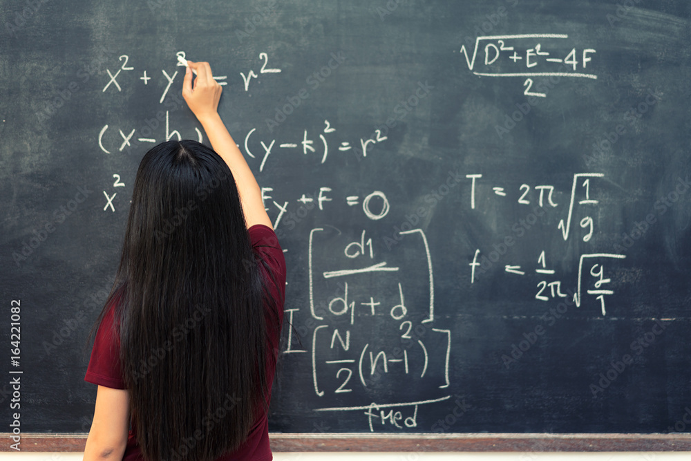 Beautiful Asian student writing on blackboard with chalk in classroom.