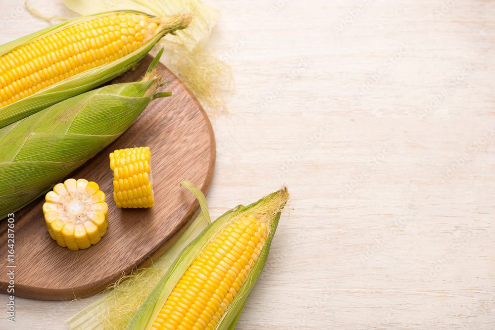 Sweet corn on cobs on cutting board on wooden table.