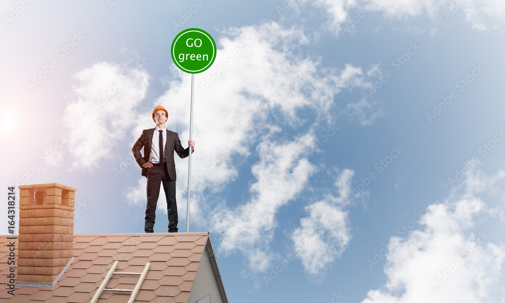 Businessman in suit on house top with ecology concept signboard. Mixed media