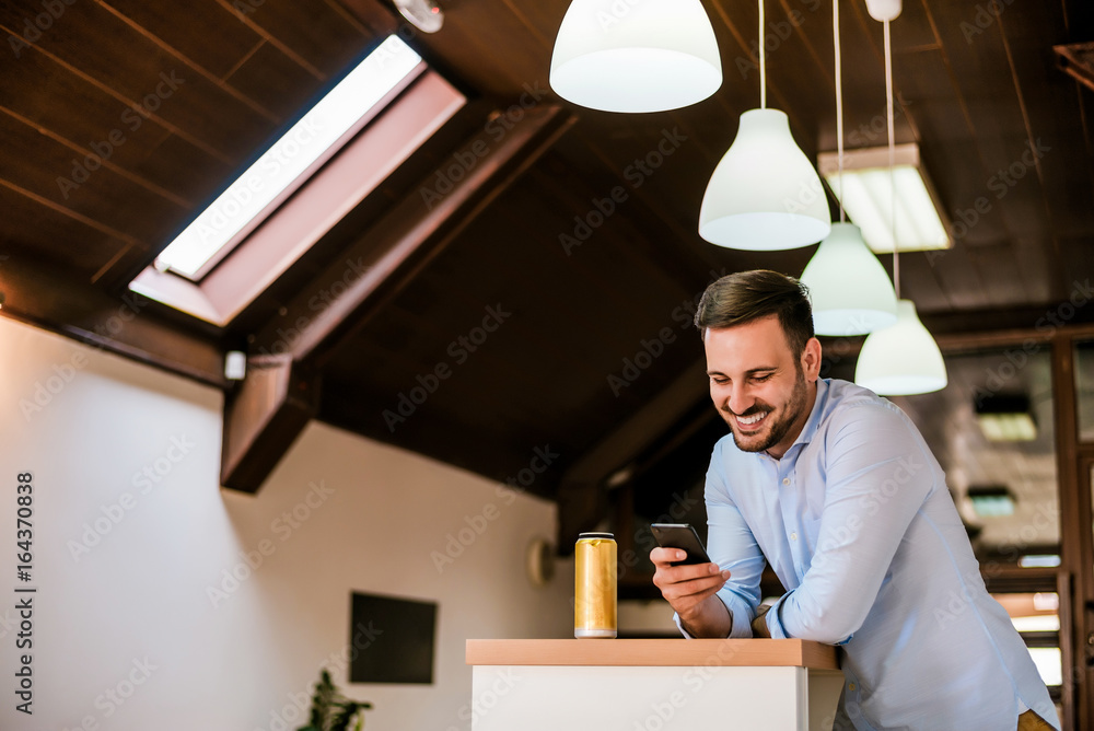 Young man holding a mobile phone and standing at the bar.