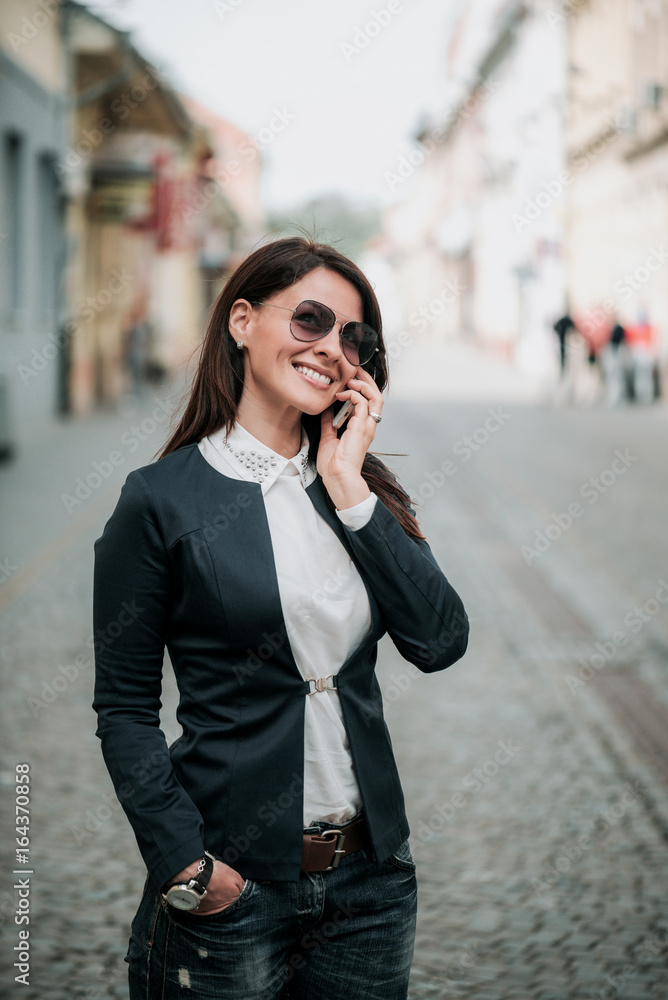 快乐的年轻女人在城市街头的生活方式画像上用手机聊天。