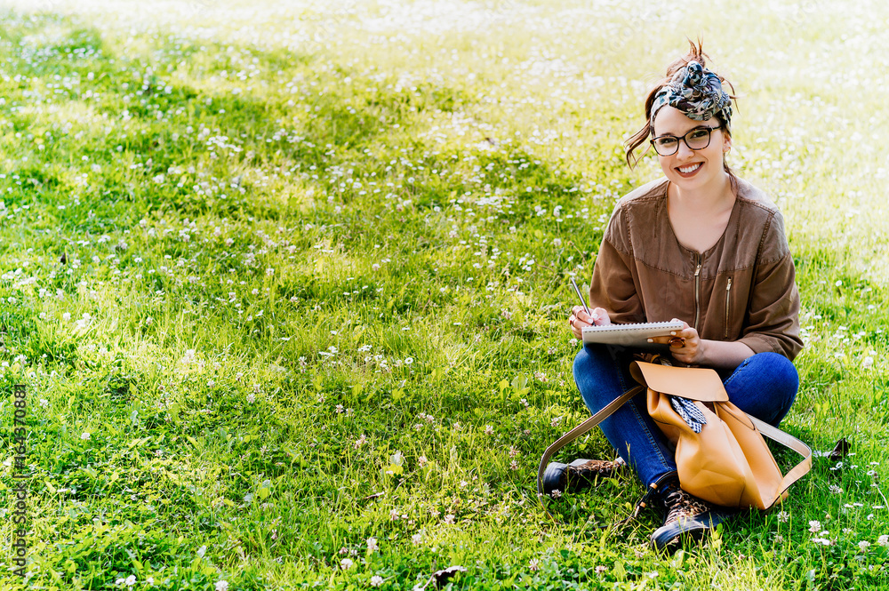 Beautiful woman with glasses writing into her diary, in the park.