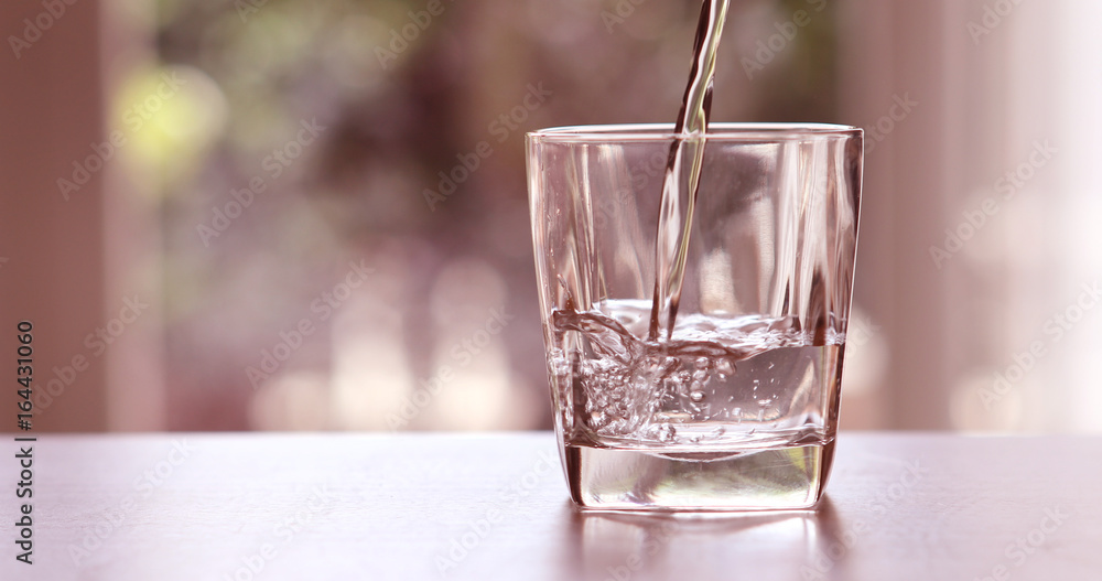 Close up pouring purified fresh drink water from the bottle on a table in living room