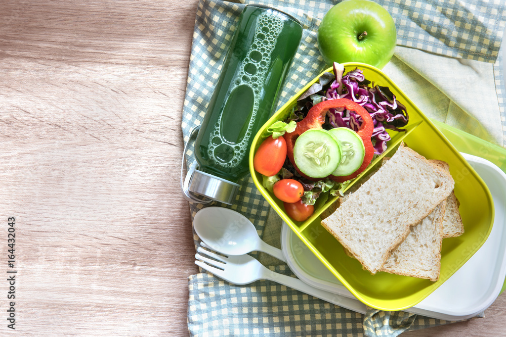 The Healthy Lunch box with grain bread and green vegetable and fruit juice bottle on wooden backgrou