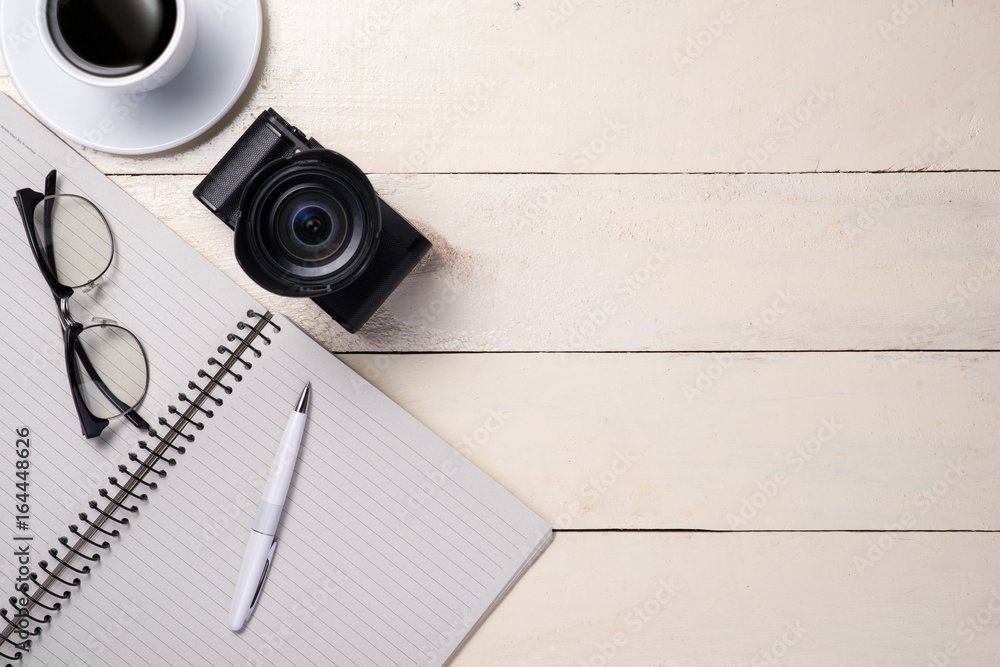 Eyeglasses, coffee, camera and notebook on table. Top view.