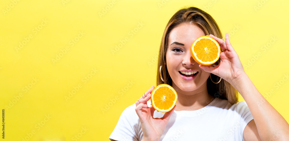 Happy young woman holding oranges halves on a yellow background