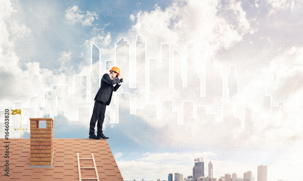 Engineer man standing on roof and looking in binoculars. Mixed m