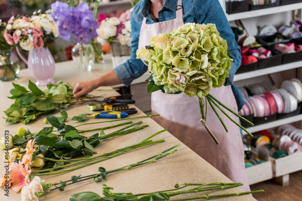 cropped shot of young florist in apron working with flowers and arranging bouquet