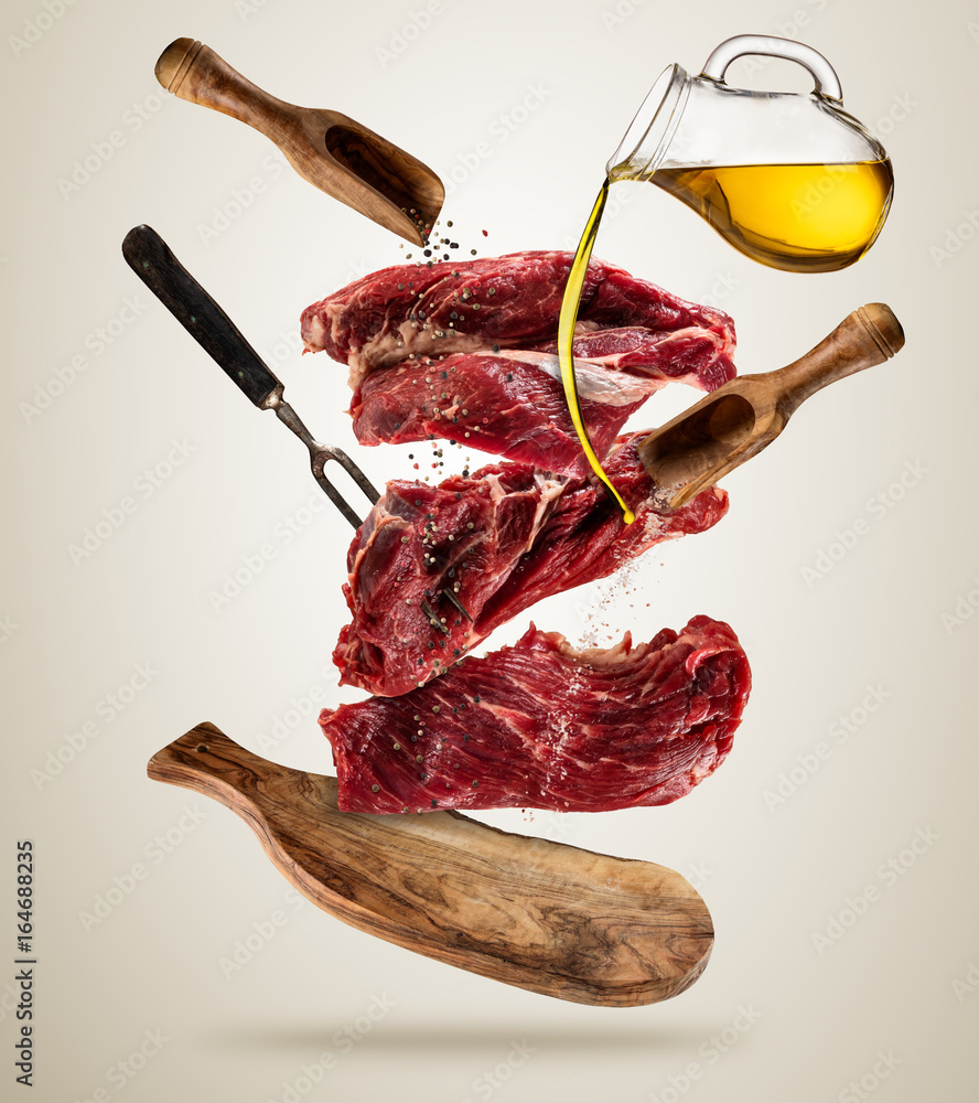 Flying raw steaks with ingredients, food preparation concept