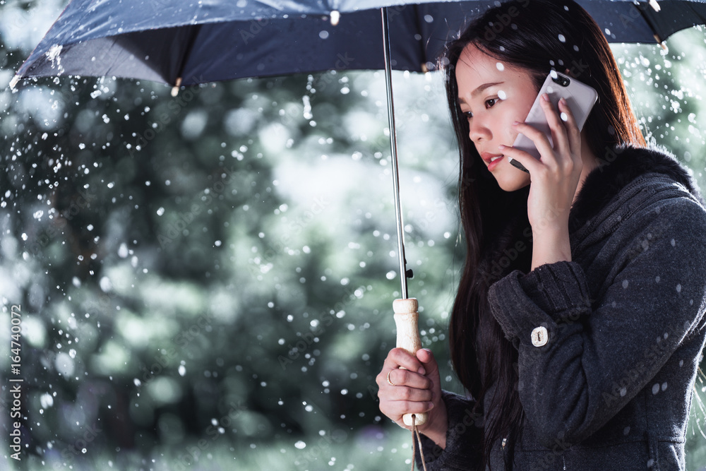 亚洲妇女正在打伞，雨正在下。她在打电话