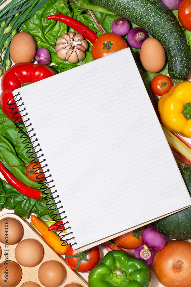 Open recipe book with fresh vegetables on wooden table.