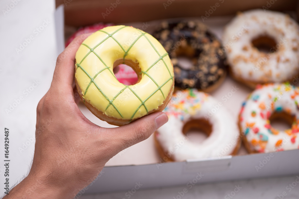 Hand holding colorful round donuts in the box