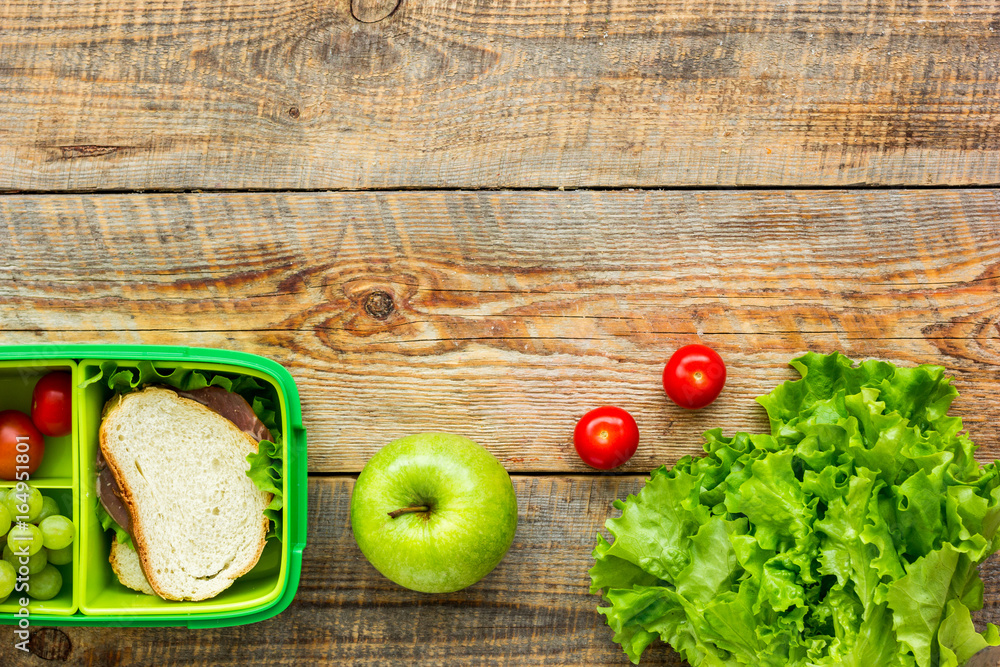 homemade lunch with apple, grape and sandwich in green lunchbox top view mockup