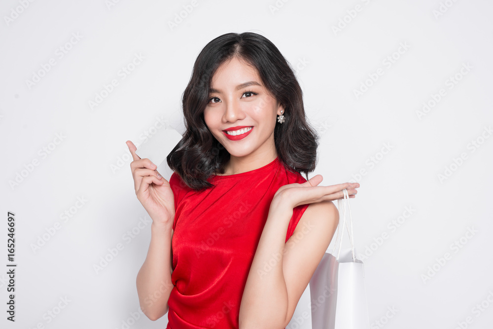 Beautiful asian woman wearing a red dress with shopping bag standing over white.