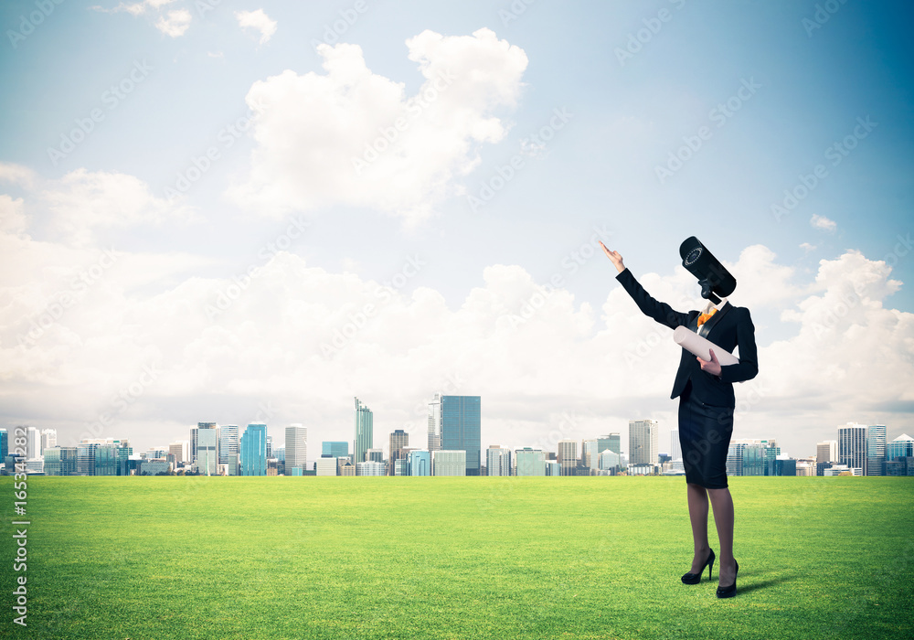 Camera headed woman standing on green grass against modern citys