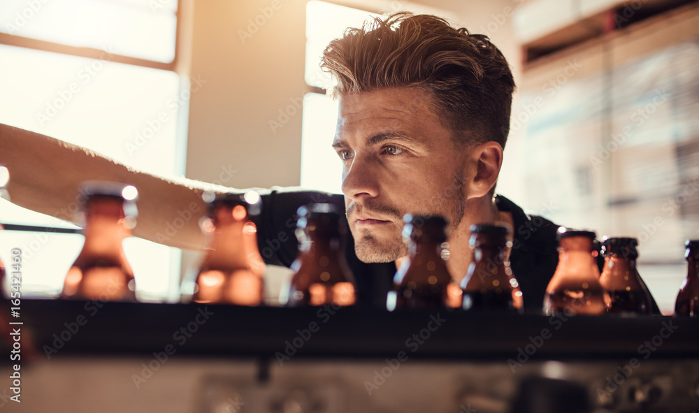 Man examining the beer bottles on conveyor at brewery factory