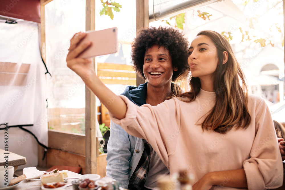 Young couple taking selfie with smart phone at cafe