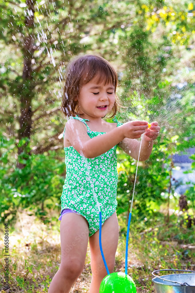 Happy toddler girl playing with sprinkler outside