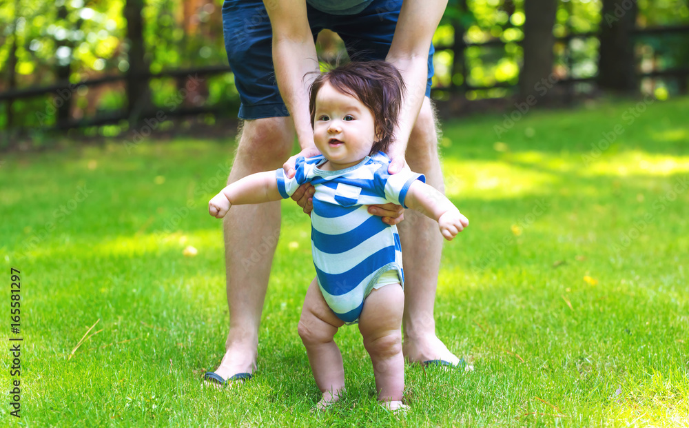 Baby boy learning to walk outside with the help of his parents