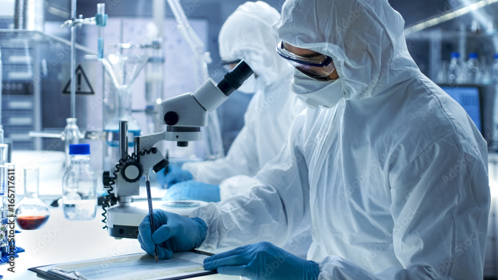 In a Secure High Level Laboratory Scientists in a Coverall Conducting a Research. Chemist Adjusts Sa