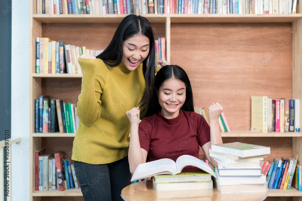 两名亚洲女学生在大学图书馆看书，很高兴能理解这节课。