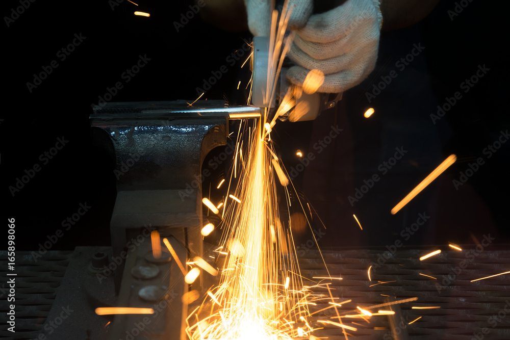 Worker cutting with grinder and welding metal with many sharp sparks in factory