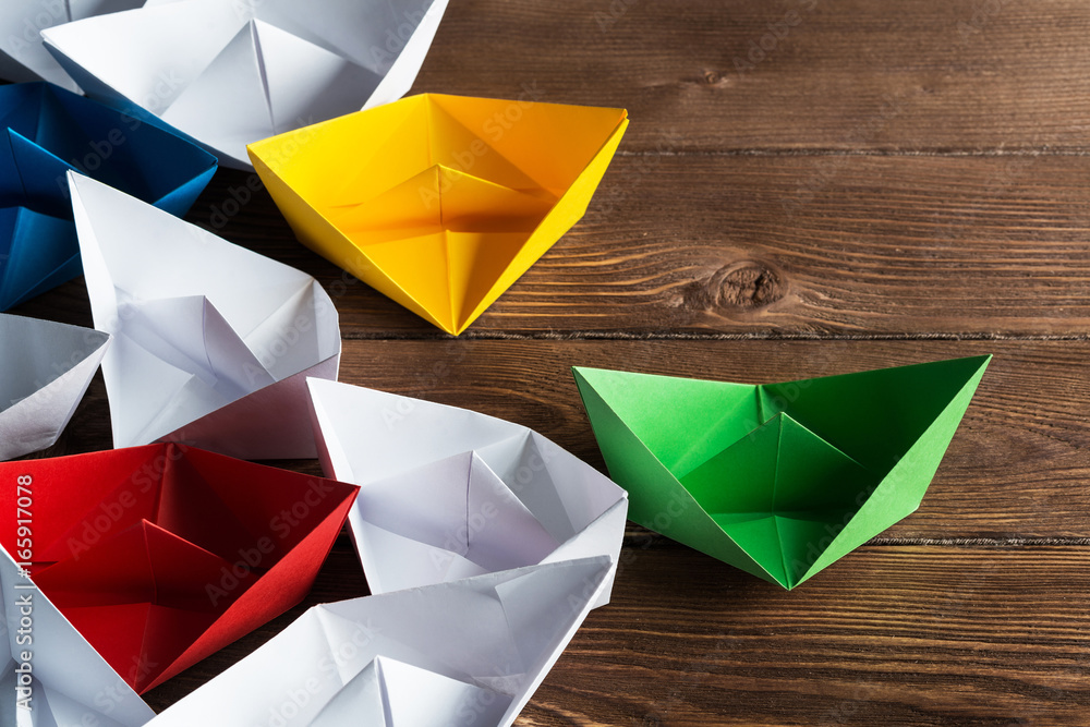 Business leadership concept with white and color paper boats on wooden table