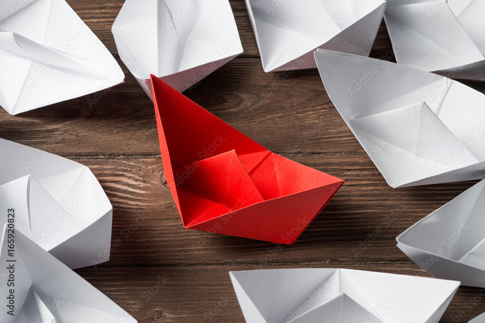 Business leadership concept with white and color paper boats on wooden table