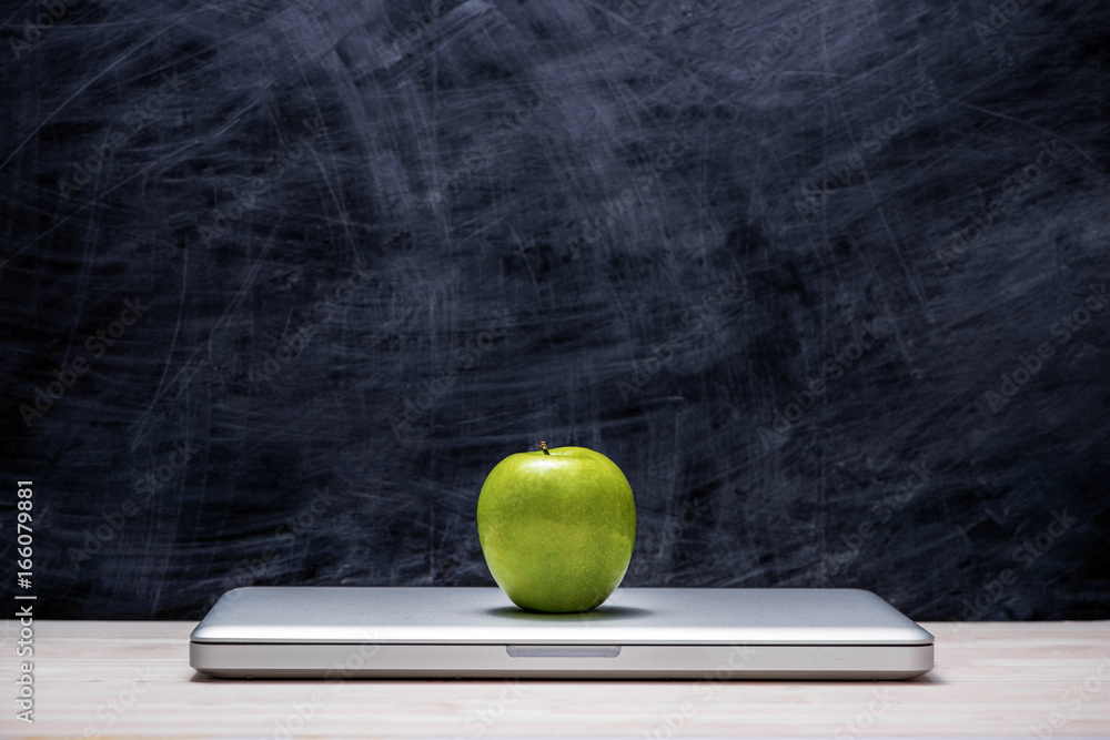 Apple on laptop on table in front of chalkboard.