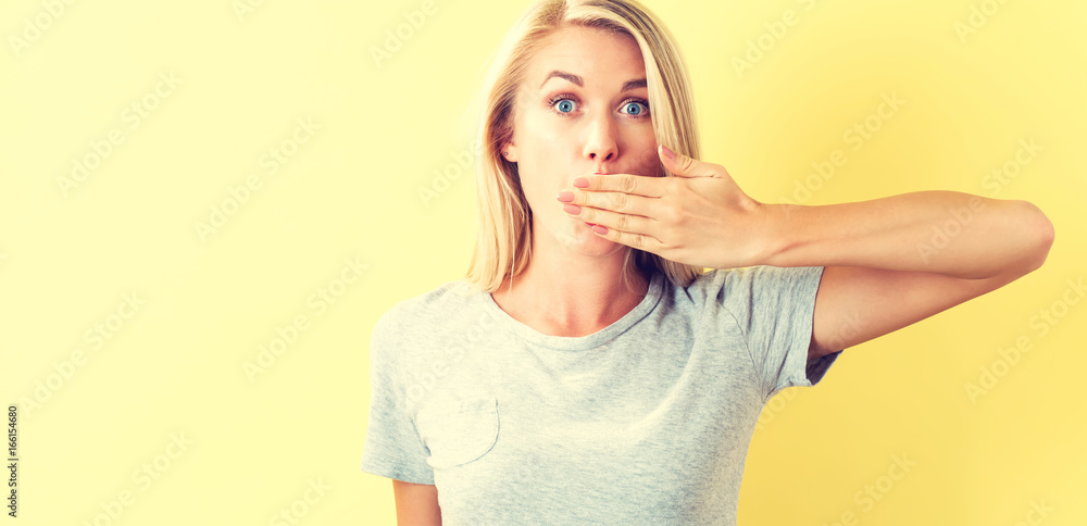 Young woman covering her mouth on a yellow background