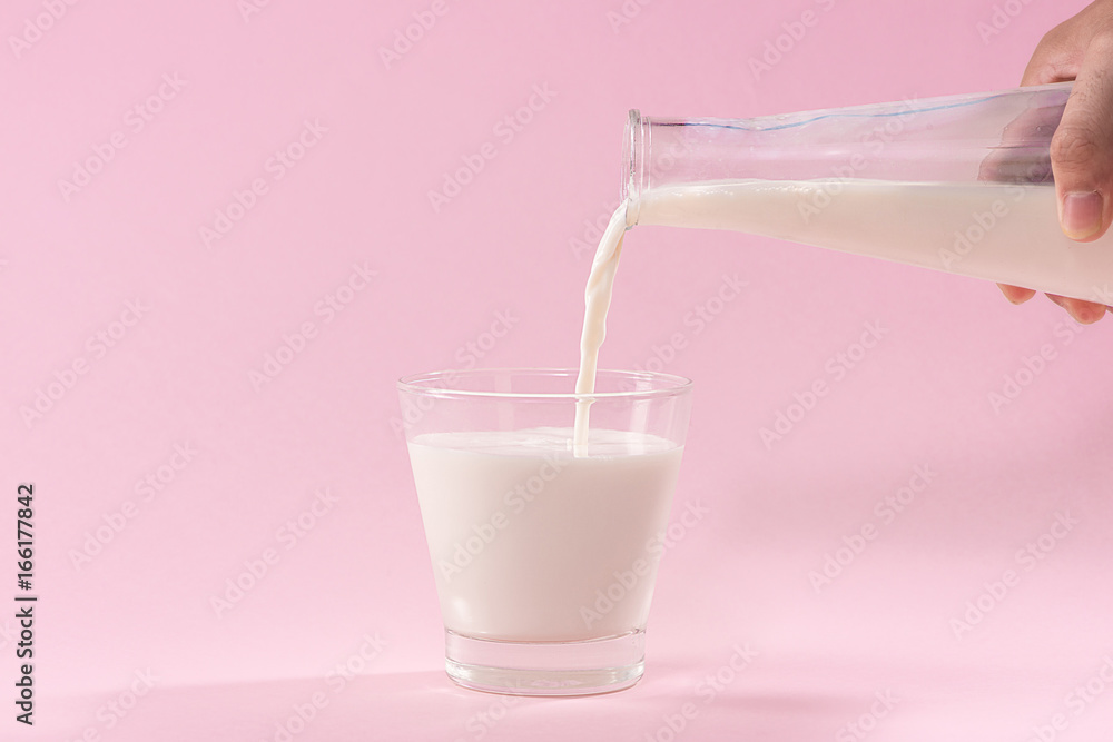 Pouring milk in to glass from bottle on a pink