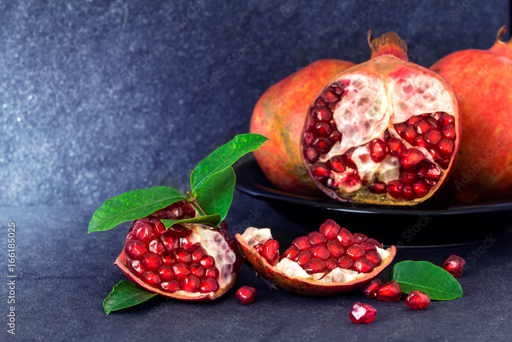 Fresh red pomegranate and seed  with leaves over black stone background