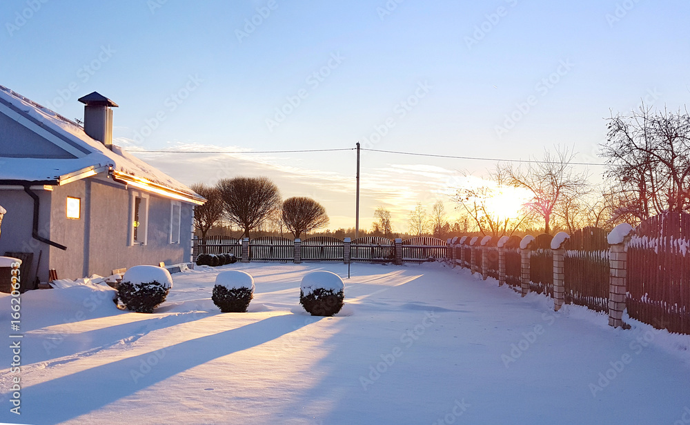 城外冬天美丽的日出。阳光下雪地下的小屋。乡村草坪