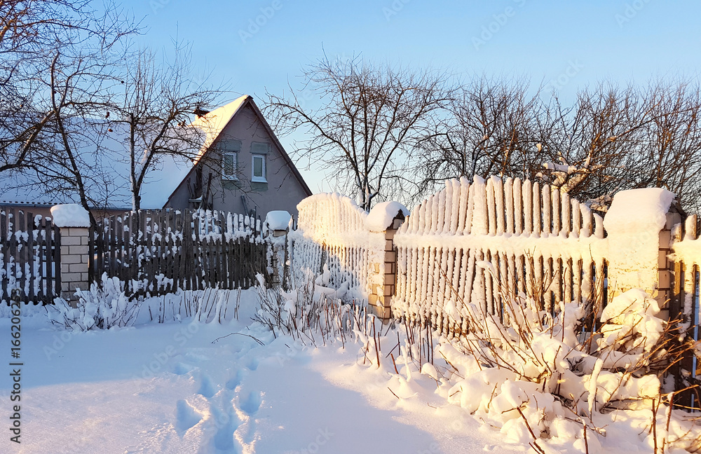 城外的冬季美丽日出。阳光下雪地下的小屋。乡村围栏