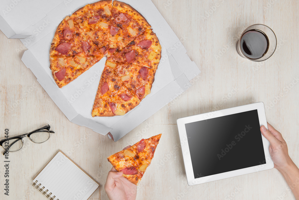 Top view image. Fast pizza delivery. Man eating and using a tablet